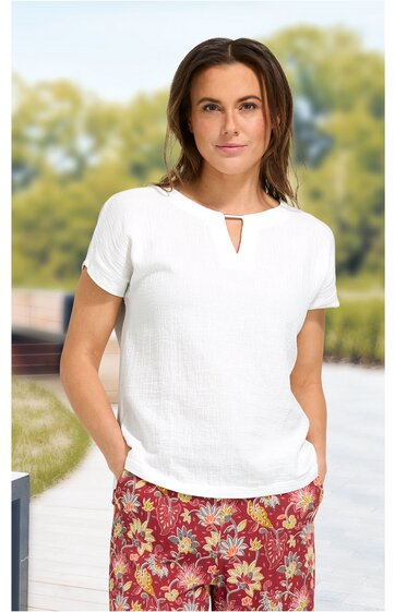 Kurzärmeliges, weißes Damenoberteil mit rundem Ausschnitt und kleinem V-förmigem Schlitz, locker sitzend, getragen von stehender Frau