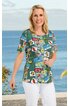 Kurzärmeliges Damenoberteil in Blau mit buntem Patchworkmuster aus Schriftzügen und Blüten, rundem Ausschnitt, gerade Form, getragen von stehender Frau vor Meereskulisse