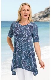 Blaues Tunika-Oberteil mit dunkelblauem Blattmuster, rundem Ausschnitt, kurze Ärmel, asymmetrischer Saum, getragen von stehender Frau am Strand