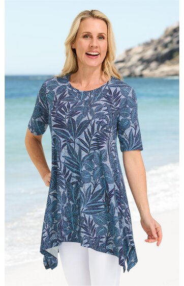 Blaues Tunika-Oberteil mit dunkelblauem Blattmuster, rundem Ausschnitt, kurze Ärmel, asymmetrischer Saum, getragen von stehender Frau am Strand