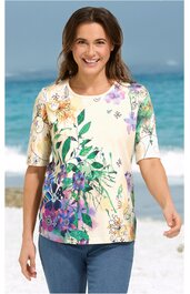 Kurzärmeliges Shirt in Creme mit buntem Blumenmuster in Grün, Lila, Orange und Gelb, Rundhalsausschnitt, gerade geschnitten, getragen von lachender stehender Frau am Strand