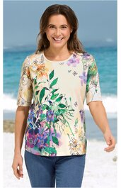 Kurzärmeliges Shirt in Creme mit buntem Blumenmuster in Grün, Lila, Orange und Gelb, Rundhalsausschnitt, gerade geschnitten, getragen von lachender stehender Frau am Strand