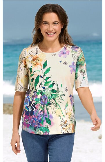 Kurzärmeliges Shirt in Creme mit buntem Blumenmuster in Grün, Lila, Orange und Gelb, Rundhalsausschnitt, gerade geschnitten, getragen von lachender stehender Frau am Strand