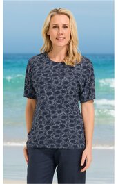 Dunkelblaues Damen-T-Shirt mit rundem Ausschnitt, kurzen Ärmeln, weißem Blumenmuster, gerade geschnitten, getragen von stehender Frau vor Meereskulisse
