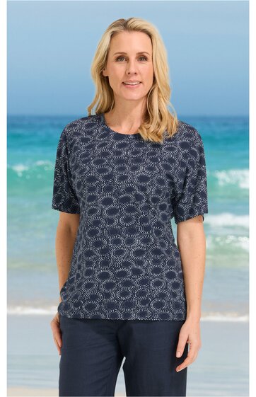 Dunkelblaues Damen-T-Shirt mit rundem Ausschnitt, kurzen Ärmeln, weißem Blumenmuster, gerade geschnitten, getragen von stehender Frau vor Meereskulisse