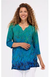 Tunika in grün und blau mit integriertem abstraktem Muster, V-Ausschnitt, dreiviertellange Ärmel, seitliche Schlitze, getragen von stehender Frau mit lockigem Haar, gerade geschnitten