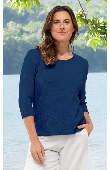Damenoberteil, marineblau, einfarbig, Rundhalsausschnitt, dreiviertellange Ärmel, leicht tailliert, getragen von stehender Frau vor See und bewaldeter Bergkulisse