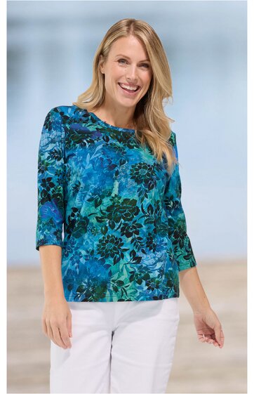 Damenbluse in Blau und Türkis mit floralem Muster, Rundhalsausschnitt, drei Viertel langen Ärmeln, gerade geschnitten, getragen von lächelnder Frau in weißer Hose, vorn locker fallend