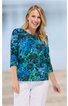 Damenbluse in Blau und Türkis mit floralem Muster, Rundhalsausschnitt, drei Viertel langen Ärmeln, gerade geschnitten, getragen von lächelnder Frau in weißer Hose, vorn locker fallend