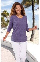 Lila langärmliges Shirt, Rundhalsausschnitt, glatte Oberfläche, getragen von lächelnder stehender Frau, kombiniert mit weißen Hosen, Freizeitkleidung