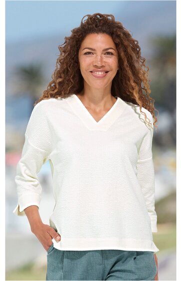 Weißes Damenoberteil mit V-Ausschnitt, 3/4-Ärmeln, kastiger Form, getragen von lächelnder Frau mit lockigen Haaren in stehender Pose