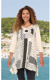 Beige Tunika mit schwarz-weiß Grafikmuster, asymmetrischer Saum, Rundhalsausschnitt, 3/4-lange Ärmel, getragen von stehender lächelnder Frau vor Landschaft mit Wasser und Häusern