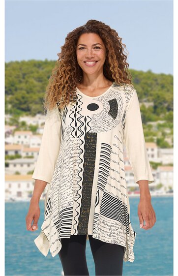 Beige Tunika mit schwarz-weiß Grafikmuster, asymmetrischer Saum, Rundhalsausschnitt, 3/4-lange Ärmel, getragen von stehender lächelnder Frau vor Landschaft mit Wasser und Häusern