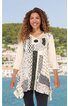 Beige Tunika mit schwarz-weiß Grafikmuster, asymmetrischer Saum, Rundhalsausschnitt, 3/4-lange Ärmel, getragen von stehender lächelnder Frau vor Landschaft mit Wasser und Häusern