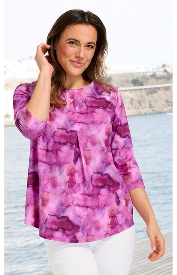 Lila und rosa gemustertes Damenoberteil mit A-Linien-Schnitt, halblangen Ärmeln, Rundhalsausschnitt, keine sichtbaren Verschlüsse, getragen von stehender Frau vor Wasserpanorama