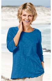 Blaues Langarmshirt ohne Muster, Rundhalsausschnitt, lockere Passform, zerzauster Saum, getragen von lächelnder stehender Frau am Strand