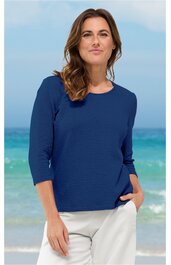 Marineblaues Langarmshirt mit Rundhalsausschnitt, taillierter Schnitt, getragen von stehender Frau vor Strandkulisse, schlichte Optik ohne sichtbare Muster oder Applikationen