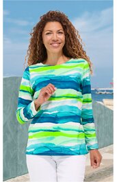 Langärmliges Shirt mit horizontalen, wellenförmigen Streifen in Weiß, Hellgrün, Türkis, Blau, Rundhalsausschnitt, gerade geschnitten, getragen von stehender Frau mit gelocktem Haar