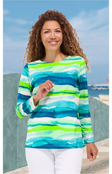 Langärmliges Shirt mit horizontalen, wellenförmigen Streifen in Weiß, Hellgrün, Türkis, Blau, Rundhalsausschnitt, gerade geschnitten, getragen von stehender Frau mit gelocktem Haar
