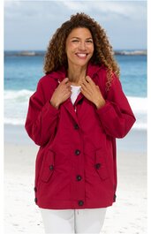 Dunkelrote Outdoorjacke mit schwarzer Knopfverschlussleiste, Klappkragen, zwei aufgesetzten Taschen mit Klappen, seitliche Knöpfe am Saum, getragen von lächelnder Frau am Strand, lange Ärmel, lockere Passform