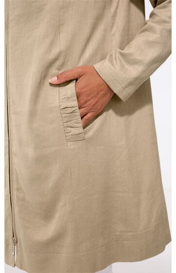 Beiger Mantel mit Reißverschluss, mittellang, durchgehend angenähter Seitentasche mit Raffung, schmal geschnitten, getragen von stehender Person mit Hand in Tasche