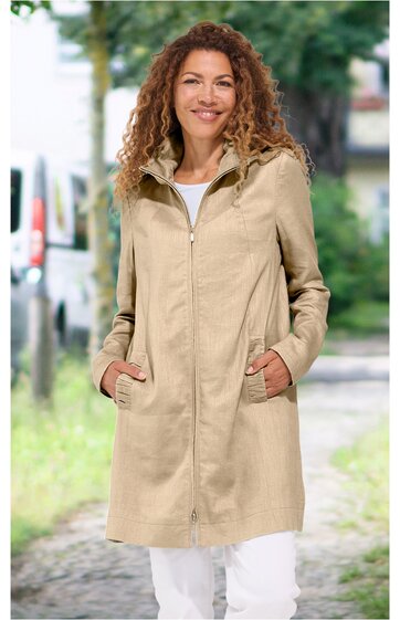 Beiger langer Mantel, gerade geschnitten, mit Stehkragen, durchgehendem Reißverschluss, seitlichen Taschen, getragen von stehender Frau mit lockigen roten Haaren