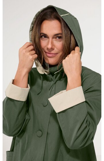 Olivgrüner Regenmantel mit beigen Ärmelumschlägen, Kapuze mit Kordelzug, Druckknöpfe vorne, getragen von frontal sichtbarer Frau, lange Ärmel