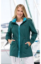 Dunkelgrüne Damenjacke mit türkisfarbenem Stehkragen, durchgehendem Reißverschluss, Tunnelzug in der Taille, langen Ärmeln, zwei seitlichen Taschen, getragen von lächelnder stehender Frau vor Wassersportkulisse