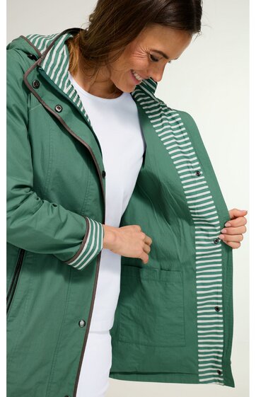 Damenregenjacke in grün, innenfutter mit weiß-grünen Streifen, Kapuze mit Kordelzug, durchgehender Reißverschluss, Druckknöpfe, getragen von stehender Frau, langärmelig