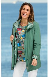 Waldgrüne Damenjacke mit durchgehender Knopfleiste, Kapuze, seitlichen Taschen, längerer taillierter Schnitt, getragen von lächelnder Frau mit dunkelblonden Haaren, darunter mehrfarbiges T-Shirt mit Aufdruck, weiße Hose