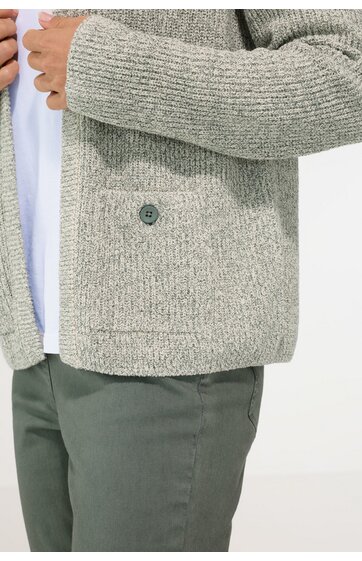Hellgrauer Strickcardigan mit grober Maschenstruktur, aufgesetzte Tasche mit Knopf auf Hüfthöhe, getragen von Person mit grüner Hose und weißem Unterhemd