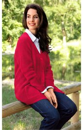 Roter Strickpullover mit V-Ausschnitt, lange Ärmel, getragen von sitzender Frau, weißes Hemd darunter, dunkelblaue Jeans, entspannte Haltung auf Holzgeländer im Freien