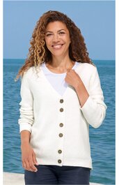 Weißer Damenstrickcardigan mit V-Ausschnitt und sechs braunen Knöpfen, langärmlig, gerade geschnitten, getragen von lächelnder Frau vor Meereskulisse