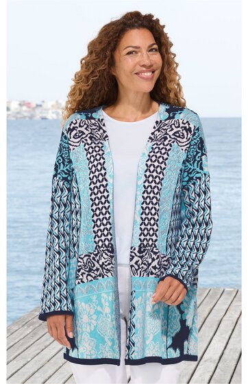 Lang geschnittener Cardigan in Hellblau und Weiß mit geometrischem und floralem Muster, offene Front ohne Verschluss, lange Ärmel, getragen von stehender Frau vor Wasserblick