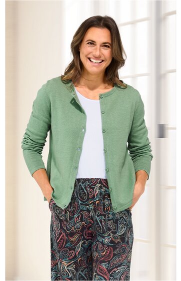 Damencardigan in salbeigrün, glatt, mit rundem Kragen, durchgehenden Knöpfen, langärmelig, getragen von lächelnder stehender Frau, offene Front, lockere Passform