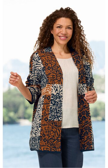 Lange Strickjacke in Braun, Dunkelblau, Beige mit abstraktem Muster, offene Front, lange Ärmel, getragen von lächelnder Frau mit lockigen Haaren, stehende Pose, helle Bluse und dunkle Hose darunter