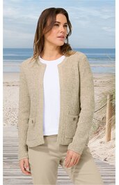 Beige Strickjacke ohne Verschluss, strukturierte Oberfläche, mit rundem Ausschnitt, langen Ärmeln, zwei aufgesetzten Taschen vorne, getragen von stehender Frau am Strand, kombiniert mit weißem Rundhalsausschnitt-Shirt und beigefarbenen Hosen