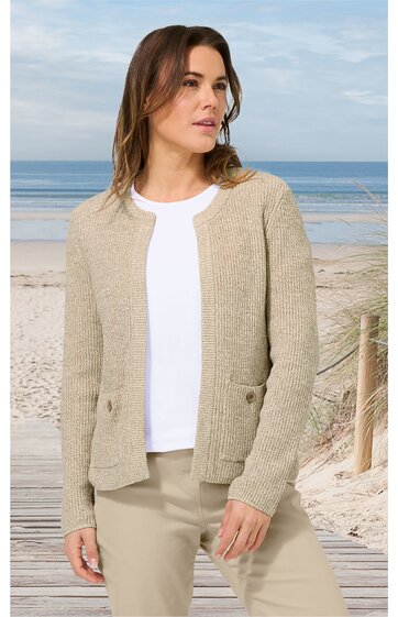 Beige Strickjacke ohne Verschluss, strukturierte Oberfläche, mit rundem Ausschnitt, langen Ärmeln, zwei aufgesetzten Taschen vorne, getragen von stehender Frau am Strand, kombiniert mit weißem Rundhalsausschnitt-Shirt und beigefarbenen Hosen