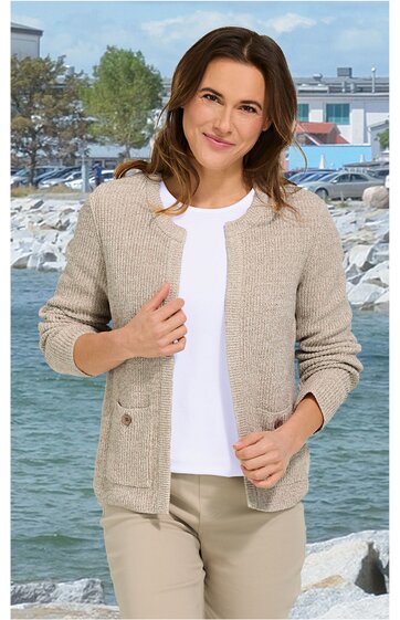 Beige Strickjacke mit Rundhals, Knopfleiste, langen Ärmeln, lockere Passform, getragen von stehender Frau vor Wasser und Felsen im Hintergrund