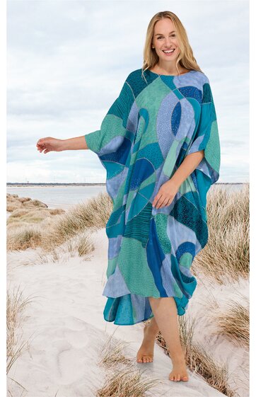 Weites Midikleid in verschiedenen Blautönen mit abstraktem Muster, Rundhalsausschnitt, weiten Ärmeln, asymmetrischem Saum, getragen von lachender Frau am Strand stehend