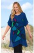 Blaues Tunika-Kleid mit abstraktem, mehrfarbigem Muster in Grün, Lila und Schwarz, V-Ausschnitt, kurze Ärmel, asymmetrischer Saum, getragen von stehender Frau am Strand