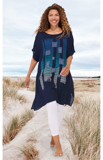 Marineblaue Tunika mit geometrischem Muster in Blau- und Türkistönen, locker sitzend, kurze Fledermausärmel, asymmetrischer Saum, getragen von stehender Frau am Strand, lang, ohne Schuhe