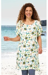 Weißes Kleid mit floralem Muster in Grün und Gelb, rundem Ausschnitt, kurze Ärmel, knielang, gerade geschnitten, getragen von lächelnder Frau, stehend am Strand