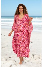 Maxikleid, pink mit roten und weißen Blattmustern, V-Ausschnitt, weite Fledermausärmel, locker sitzend, getragen von stehender Frau am Strand