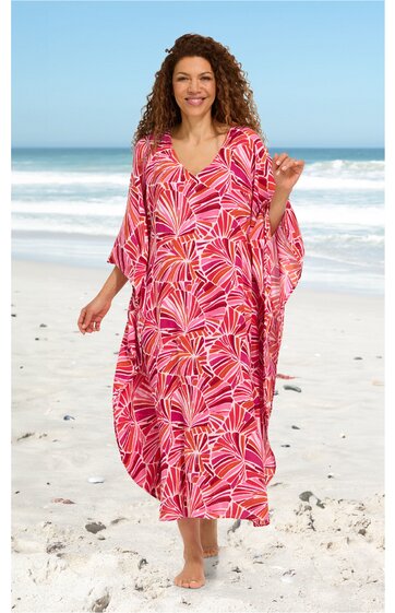 Maxikleid, pink mit roten und weißen Blattmustern, V-Ausschnitt, weite Fledermausärmel, locker sitzend, getragen von stehender Frau am Strand