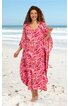 Maxikleid, pink mit roten und weißen Blattmustern, V-Ausschnitt, weite Fledermausärmel, locker sitzend, getragen von stehender Frau am Strand