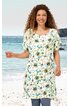 Weißes Kleid mit floralem Muster in Grün und Gelb, rundem Ausschnitt, kurze Ärmel, knielang, gerade geschnitten, getragen von lächelnder Frau, stehend am Strand