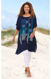 Dunkelblaues Tunika-Kleid mit rechteckigem Muster in Hellblau und Weiß, U-Boot-Ausschnitt, lockere Passform, kurzärmlig, getragen von lächelnder stehender Frau am Strand, knielang