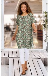 Grünes Tunika-Kleid mit floralem Muster in Beige und Weiß, rundem Ausschnitt, kurze Ärmel, knielang, locker geschnitten, getragen von stehender Frau, trägt weiße Leggings und braune Sandalen
