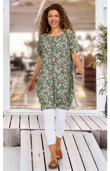 Grünes Tunika-Kleid mit floralem Muster in Beige und Weiß, rundem Ausschnitt, kurze Ärmel, knielang, locker geschnitten, getragen von stehender Frau, trägt weiße Leggings und braune Sandalen